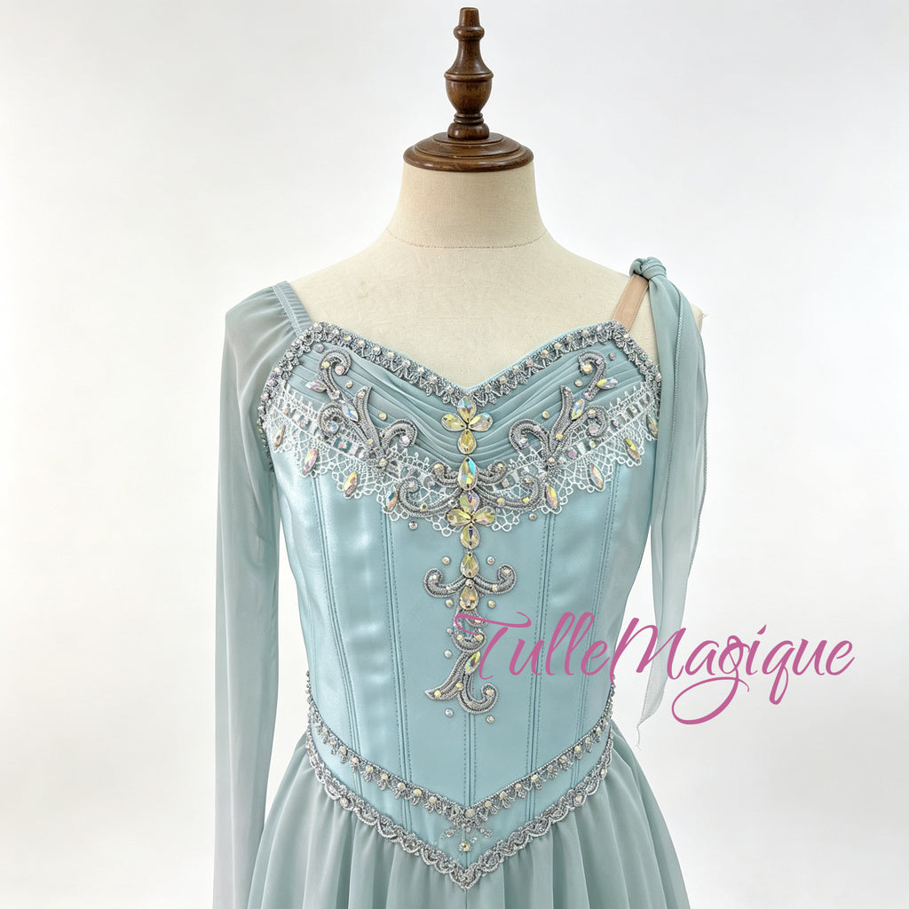 custom-made asymmetric lyrical dance dress or ice skating wear in light gradient blue, highlighting a detailed bodice with central gold and silver crystals and fluid tiered snow chiffon layers