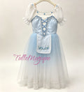 A light blue and white professional ballet romantic tutu for Giselle. The peasant dress features a light baby blue satin bodice with blue lace-up corset details, short white ruffled sleeves, a light blue satin bodice, a white apron with blue floral embroidery, and a layered blue white ombre tulle skirt.