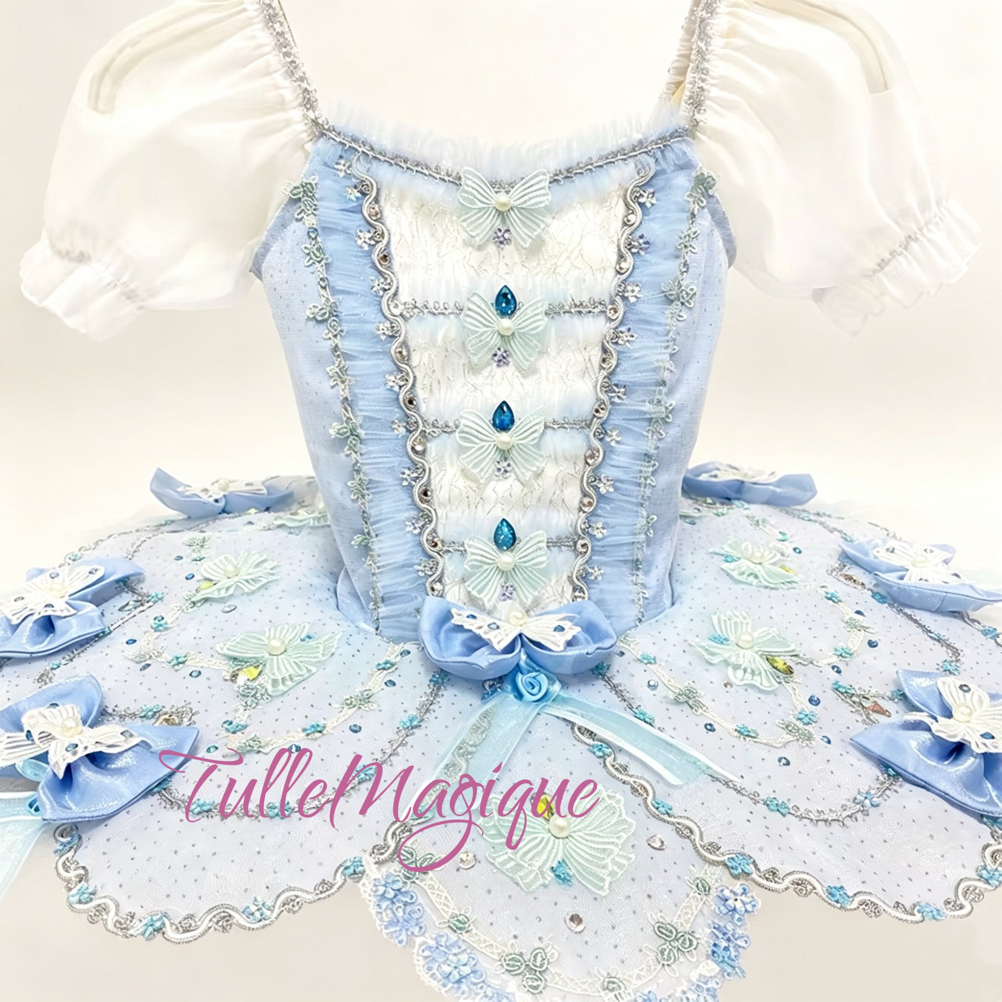 Handcrafted light blue and white ballet competition costume for Coppelia Swanilda or Breadcrumb Fairy variations, adorned with ribbon bows, fine silver trim, and a matching bow headpiece.