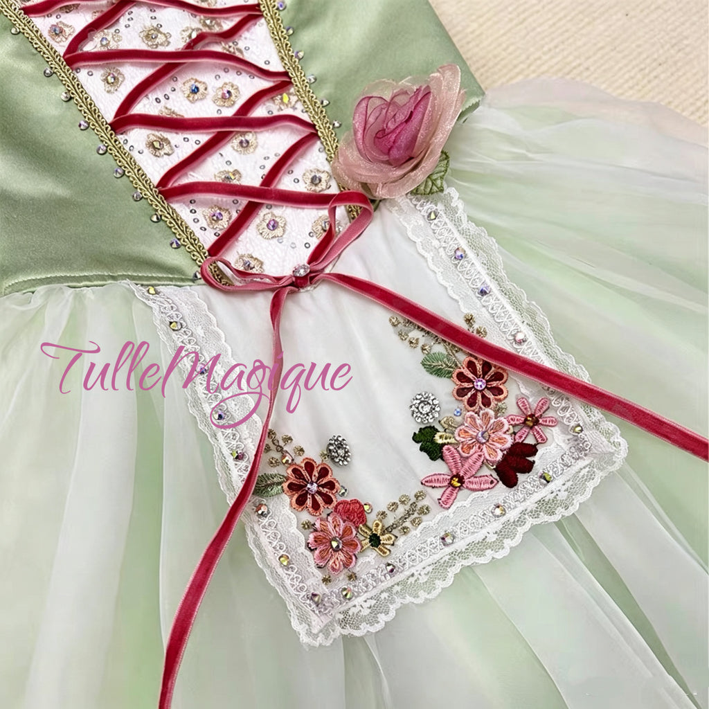 Close-up of a light sage green satin ballet bodice featuring wine red criss-cross ribbon lacing, gold trim, and a 3D pink rose accessory.