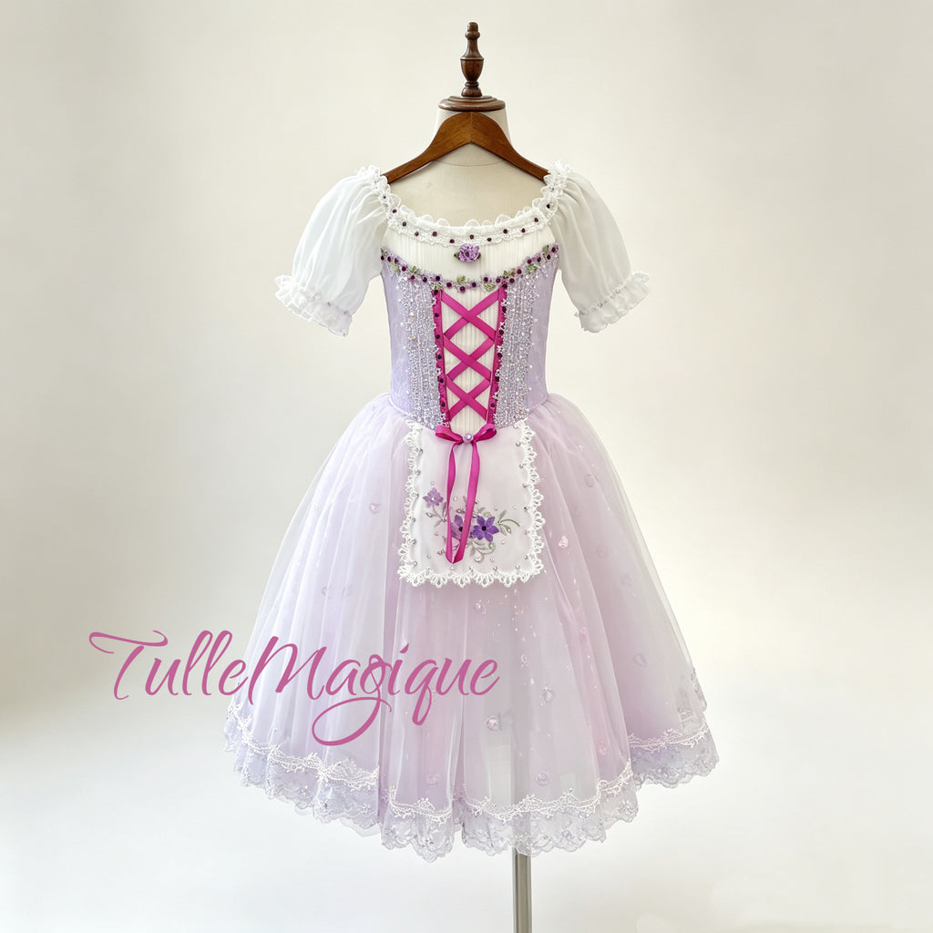 Front view of a professional lavender romantic ballet tutu featuring a lilac bodice with magenta criss-cross ribbons, an embroidered floral apron, and a lace-trimmed tulle skirt.