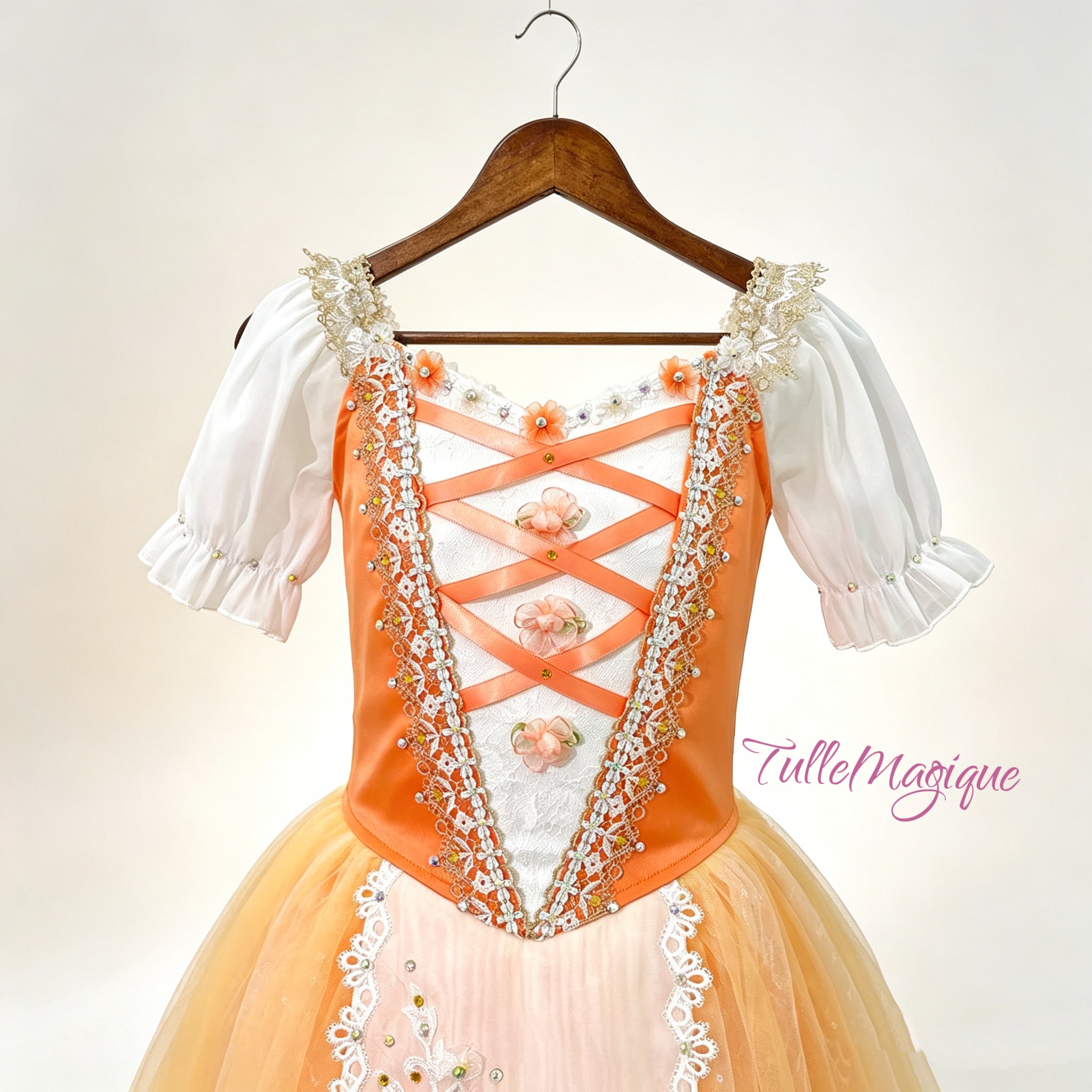 Close-up of the orange satin ballet bodice showcasing orange criss-cross ribbon lacing, delicate 3D floral accents, and intricate gold land white ace embroidery
