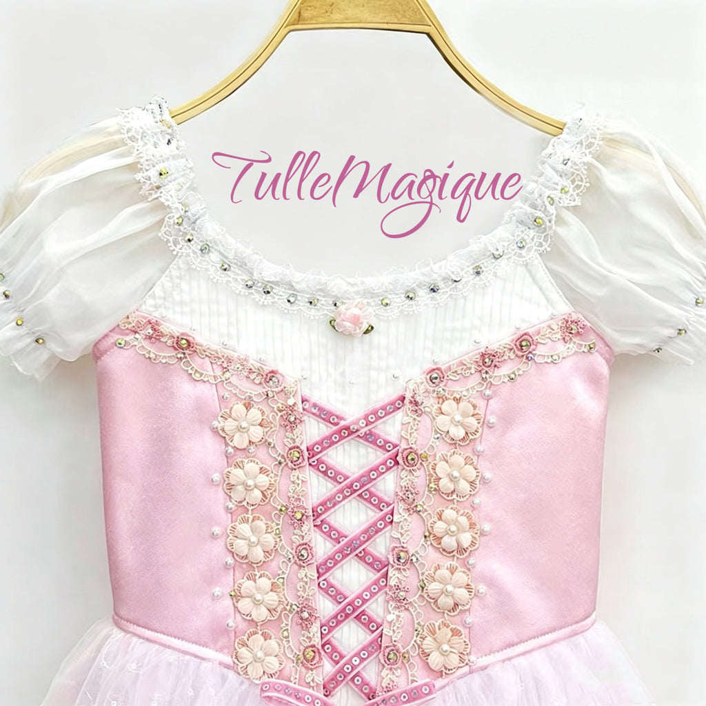 Close-up of the front bodice from the ballet costume showcasing pink satin fabric, a white pleated chiffon neckline, pink criss-cross ribbon corset lacing, and delicate floral embroidery with rhinestones.