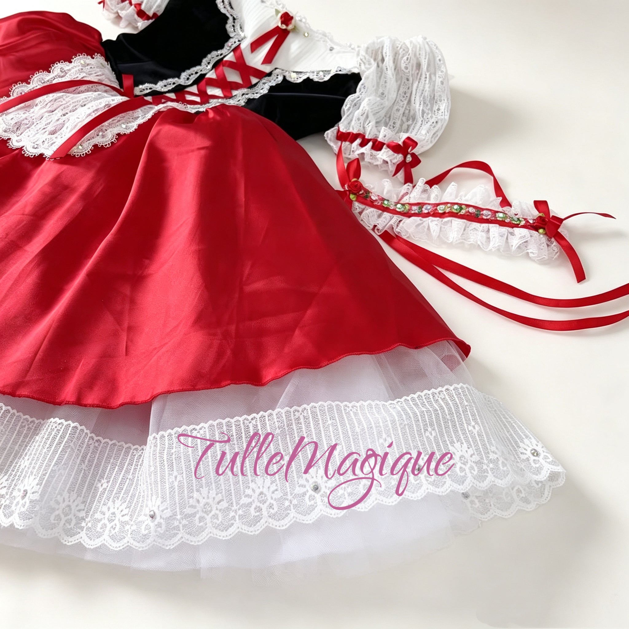Flat lay front view of a professional black velvet and red peasant ballet costume featuring red ribbon corset lacing, a rhinestone-trimmed white lace apron, and matching floral wrist accessories