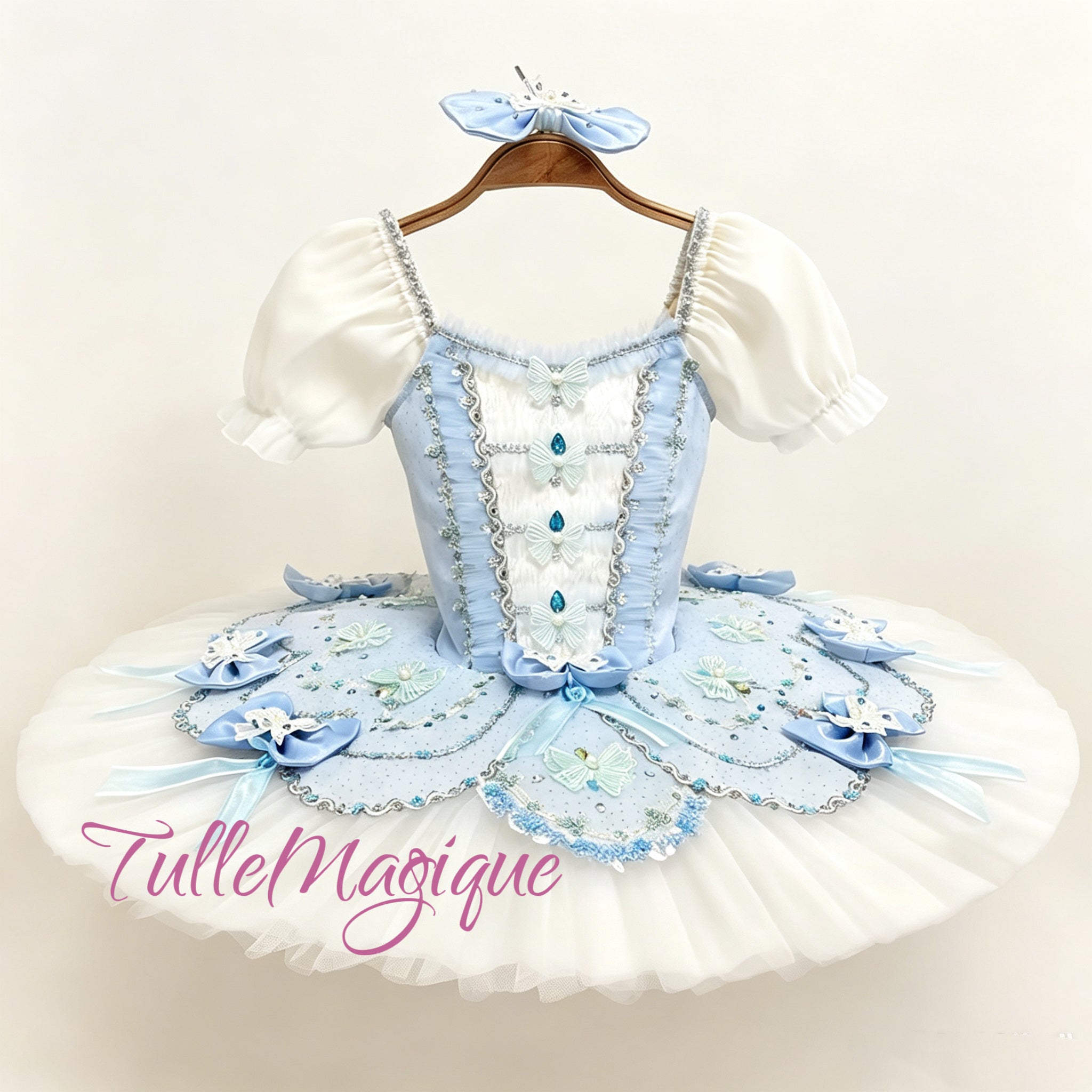Professional light blue and white classical ballet tutu for The Fairy Doll repertoire variation, featuring romantic puff sleeves, a row of vertical bodice bows with deep blue crystals, and an embroidered butterfly skirt plate for YAGP.
